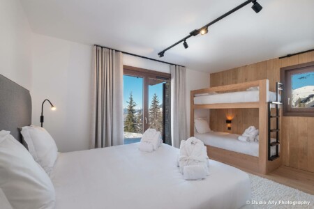 photographie agence immobilière à Courchevel : chambre avec lit adultes et lits enfants superposés en rez de jardin avec vue sur les sapins